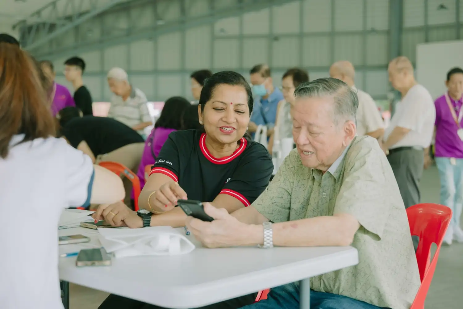 A DBS volunteer teaches a senior beneficiary on how to use a mobile phone.