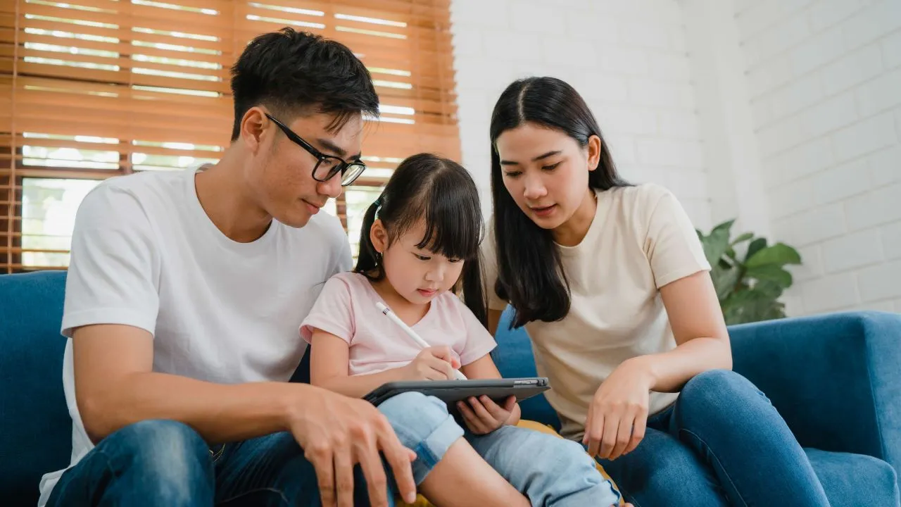 Happy asian family dad, mom and daughter using computer tablet technology sitting sofa in living room at house