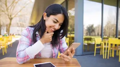 Young woman smiling at her phone at a table
