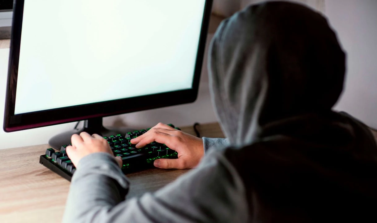 A young person seen from behind, seated at a computer with hands on the keyboard
