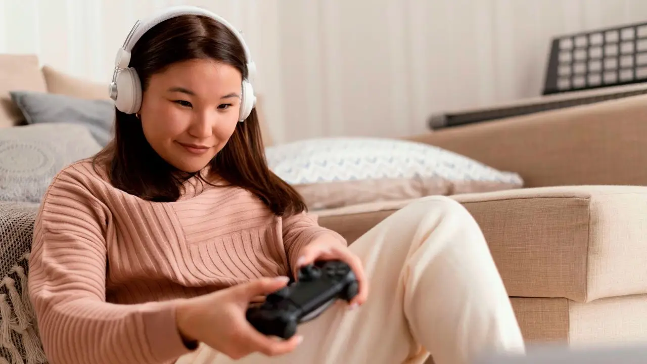 A teenage girl wearing headphones and holding a game controller while gaming indoors