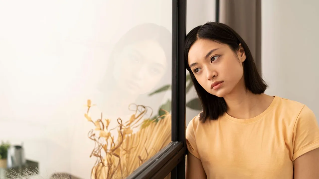 A young woman looking sad as she leans against a metal window grille
