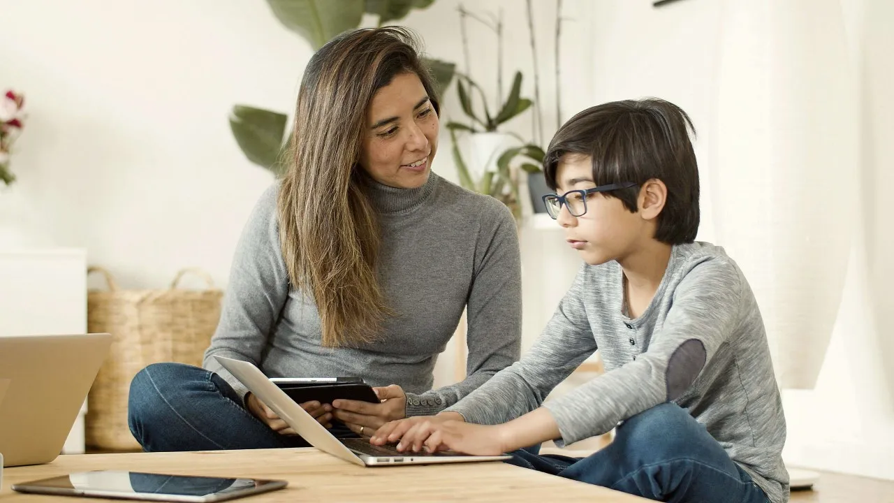 A mother speaking to a boy, using his laptop